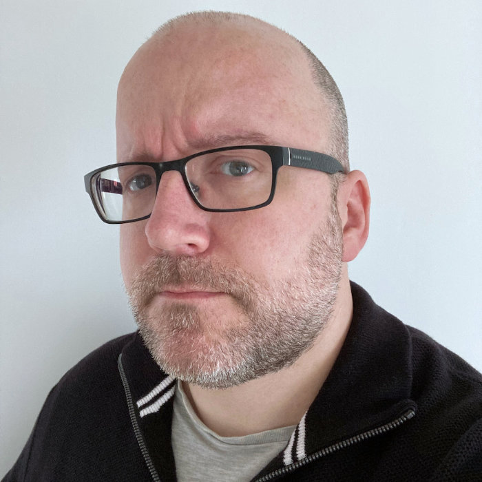 Photograph of Patrick, looking thoughtful as he's probably contemplating WACG 2.5.1, with a short, neatly trimmed beard and moustache, wearing glasses with a rectangular black frame and a slight frown